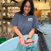 A smiling woman holding a small paddlefish over a large tub with others swimming inside