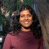 A smiling woman in a maroon shirt standing next to a tree