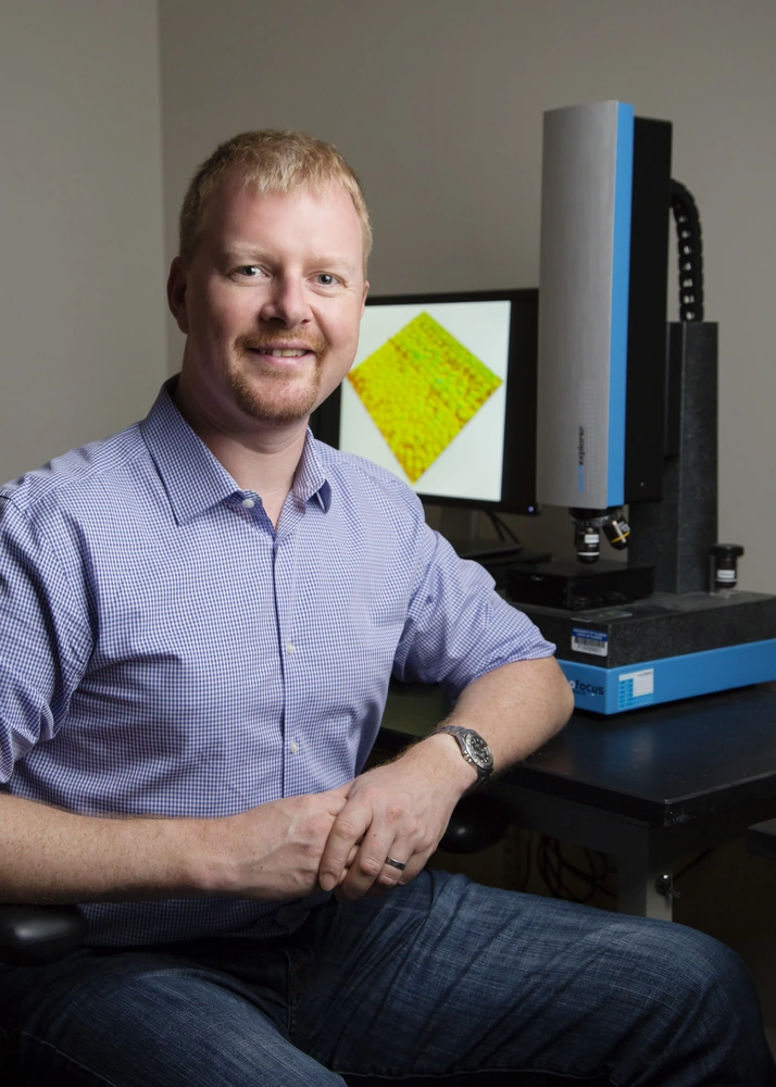 A photo of a man in a purple button up sitting next to a computer