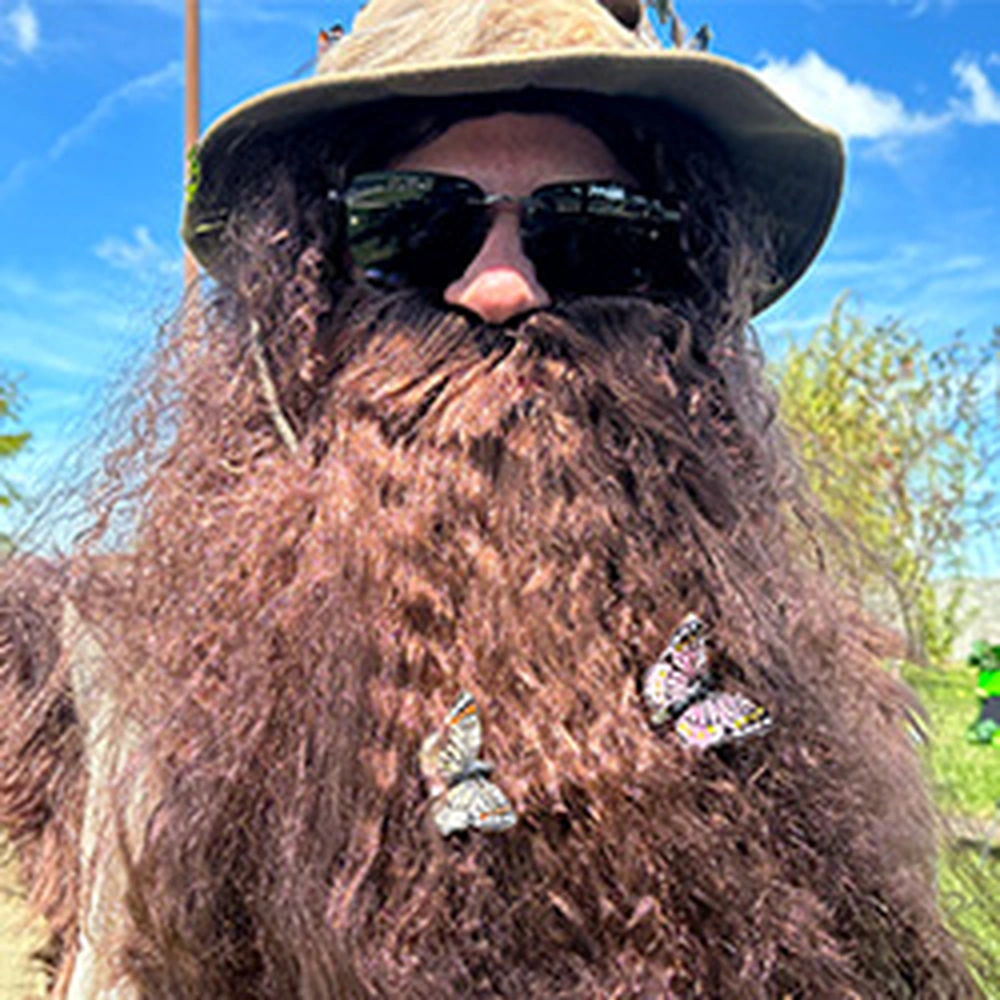 a man in a safari hat, sunglasses, and a fake beard with fake butterflies attached to it