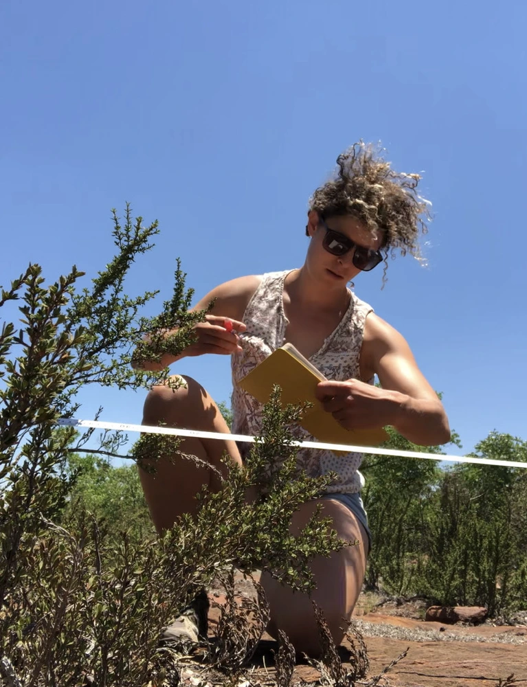 A woman crouching next to a plant outdoors