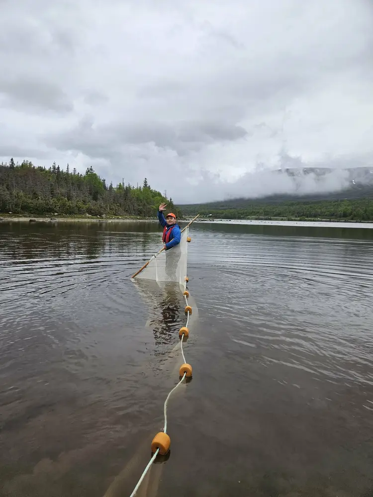 A man waving while holding a net and a rope of buoys out in water 