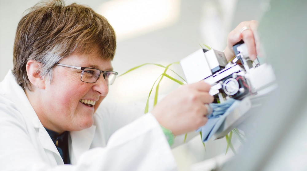 A smiling woman in a lab coat working with a piece of technology