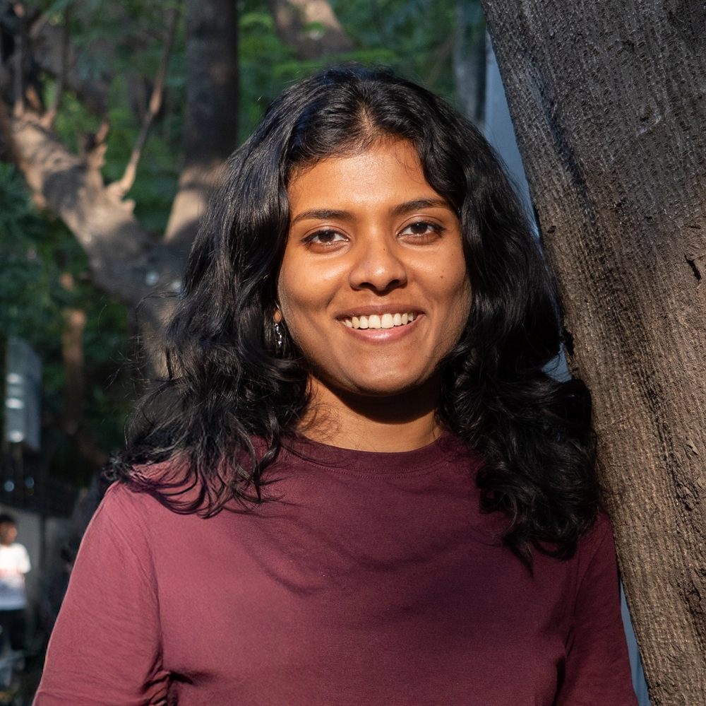 A smiling woman in a maroon shirt standing next to a tree