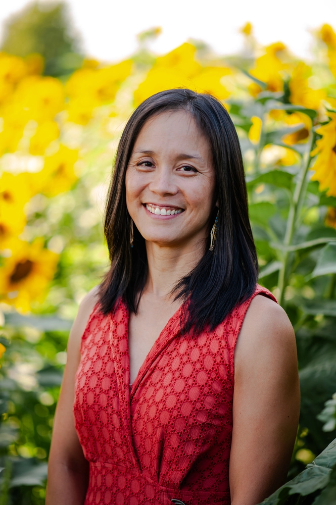 a woman smiling in a red shirt with sunflowers behind her