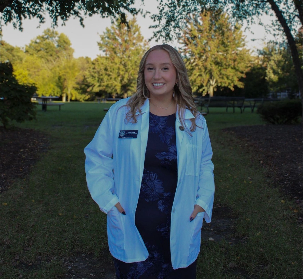 A smiling woman outside in a white lab coat