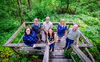 A group of people standing on a wooden platform with woods behind them