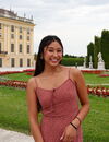 A photo of a woman in a pink dress with a grassy garden and a building behind her