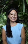 A smiling woman in a blue shirt with plants behind her
