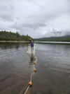 A man waving while holding a net and a rope of buoys out in water 