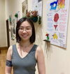 A smiling woman in a tank top standing next to posters hanging on a wall