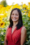 a woman smiling in a red shirt with sunflowers behind her