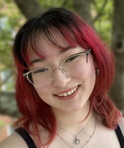 A smiling person with red hair and glasses outside