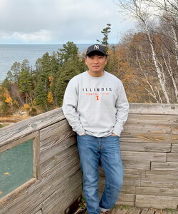 A man in a sweater standing outside by a waist-high stone wall