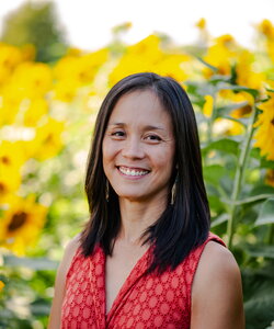 a woman smiling in a red shirt with sunflowers behind her