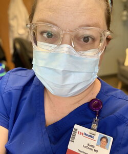A woman in a blue scrubs, a face mask, and glasses