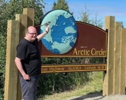 A photo of Aiden Schore next to a sign for the Arctic Circle