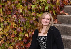 A photo of Emma Borop standing on stairs next to leaves changing colors