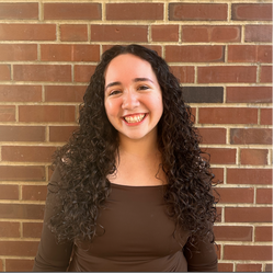 A headshot of Juliana Alvarez in front of a brick wall