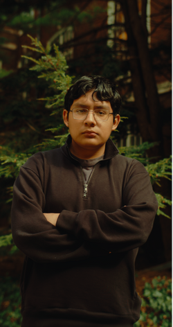 A photo of Karol Penuelas standing cross-armed in the woods