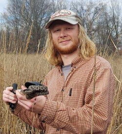 A photo of Zander Perelman holding a snake in a tall field of grass
