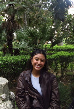 A photo of Ella Narag sitting out by some bushes and trees