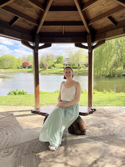 A photo of Samantha Dubbs sitting under a gazebo with a pond behind her
