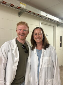 A man and a woman standing in a white hallway wearing lab coats