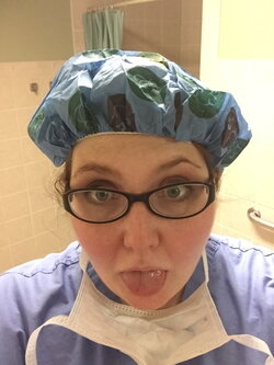 A person wearing nursing scrubs, glasses, and a mask around her neck