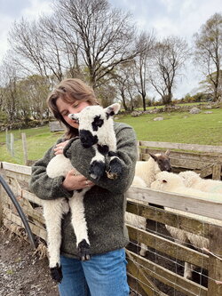 a student in a green coat holding a small lamb next to a wall