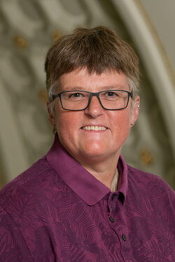 A woamn in glasses and purple collared shirt with a blurry background